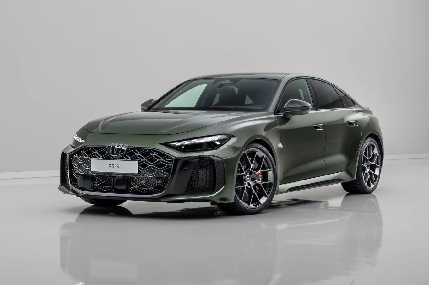 Samochód sportowy Audi RS 5 w zielonym kolorze, sfotografowany w jasnym studiu na błyszczącej podłodze. Pojazd z charakterystycznym agresywnym przodem, dużymi felgami i nowoczesnym oświetleniem LED.
