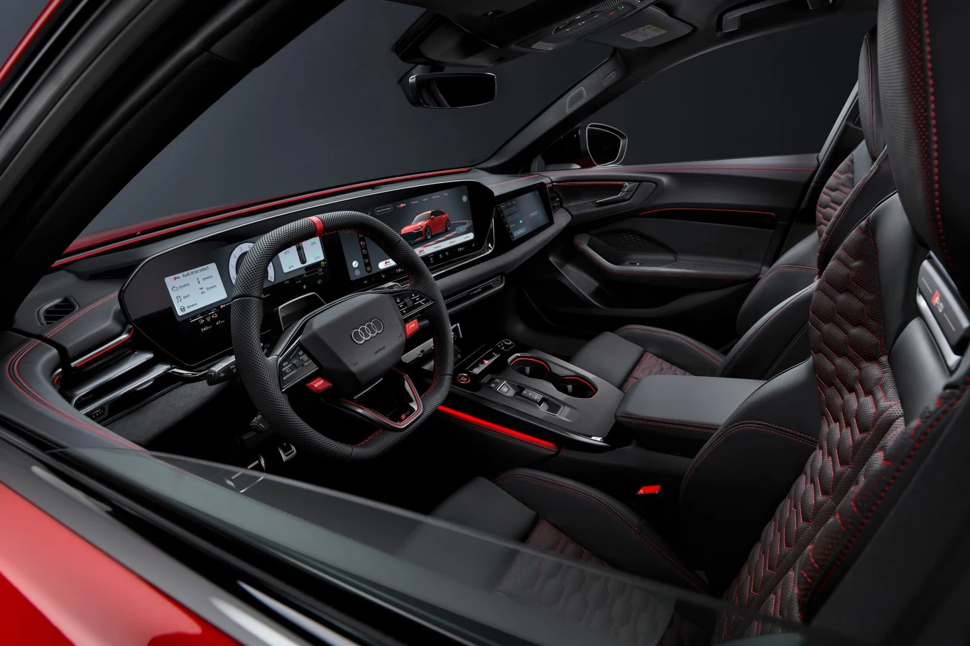 Nowoczesna, luksusowa kabina samochodu marki Audi wyposażona w elektroniczne wyświetlacze, sportowe fotele z pikowaną tapicerką oraz detale wykończenia w kolorze czerwonym.