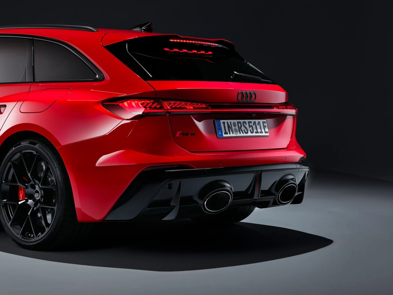 Czerwony sportowy samochód Audi RS z charakterystycznymi tylnymi światłami LED, podwójnymi końcówkami wydechu i czarnymi felgami, sfotografowany w studiu na tle czarnej ściany.