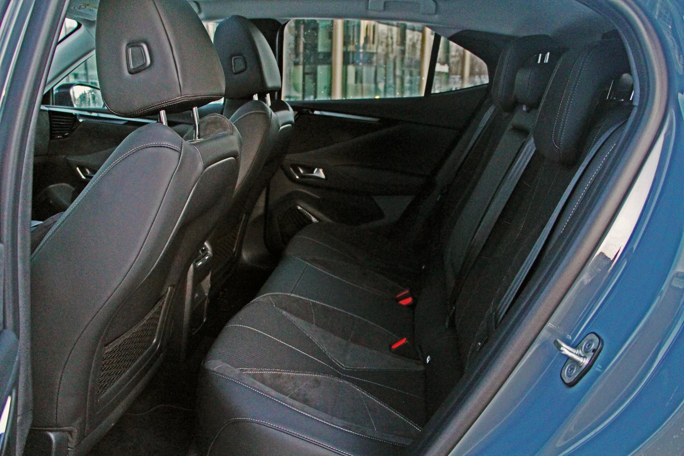 DS No4 oferuje przeciętną ilość miejsca z tyłu Wnętrze samochodu z widokiem na tylne siedzenia, czarne tapicerowane fotele, dwa zagłówki przednich siedzeń, z tyłu trzy miejsca z pasami bezpieczeństwa, widoczne wykończenie drzwi oraz kieszeń na oparciu fotela.