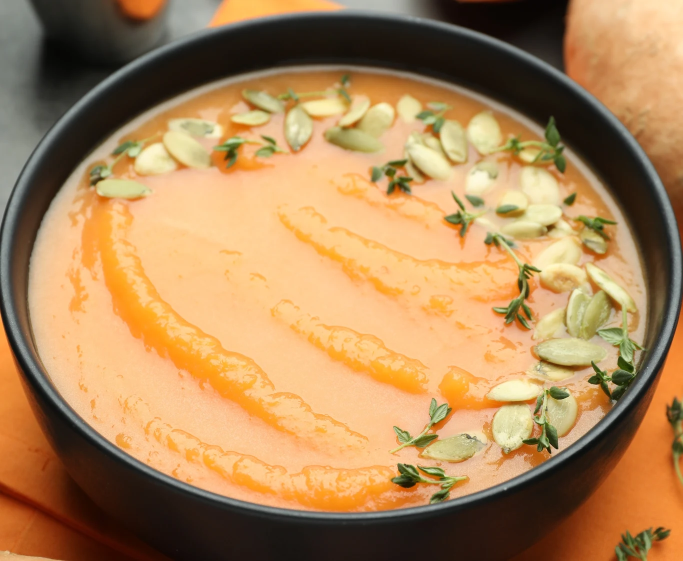 Kremowa zupa dyniowa w misce, udekorowana pestkami dyni oraz świeżymi gałązkami tymianku.