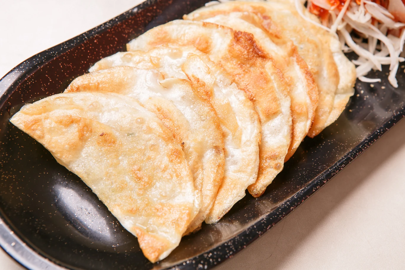 Usmażone na złoto pierogi układane jeden obok drugiego na ciemnym talerzu, obok odrobina surówki z białej kapusty i marchewki.