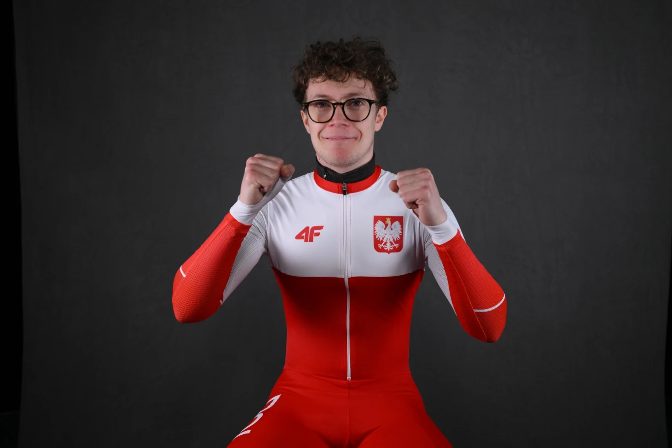 Felix Pigeon Sportowiec w stroju reprezentacji Polski, biało-czerwony kombinezon z godłem narodowym na piersi, zaciśnięte pięści uniesione w geście triumfu, ciemne tło podkreśla sylwetkę.