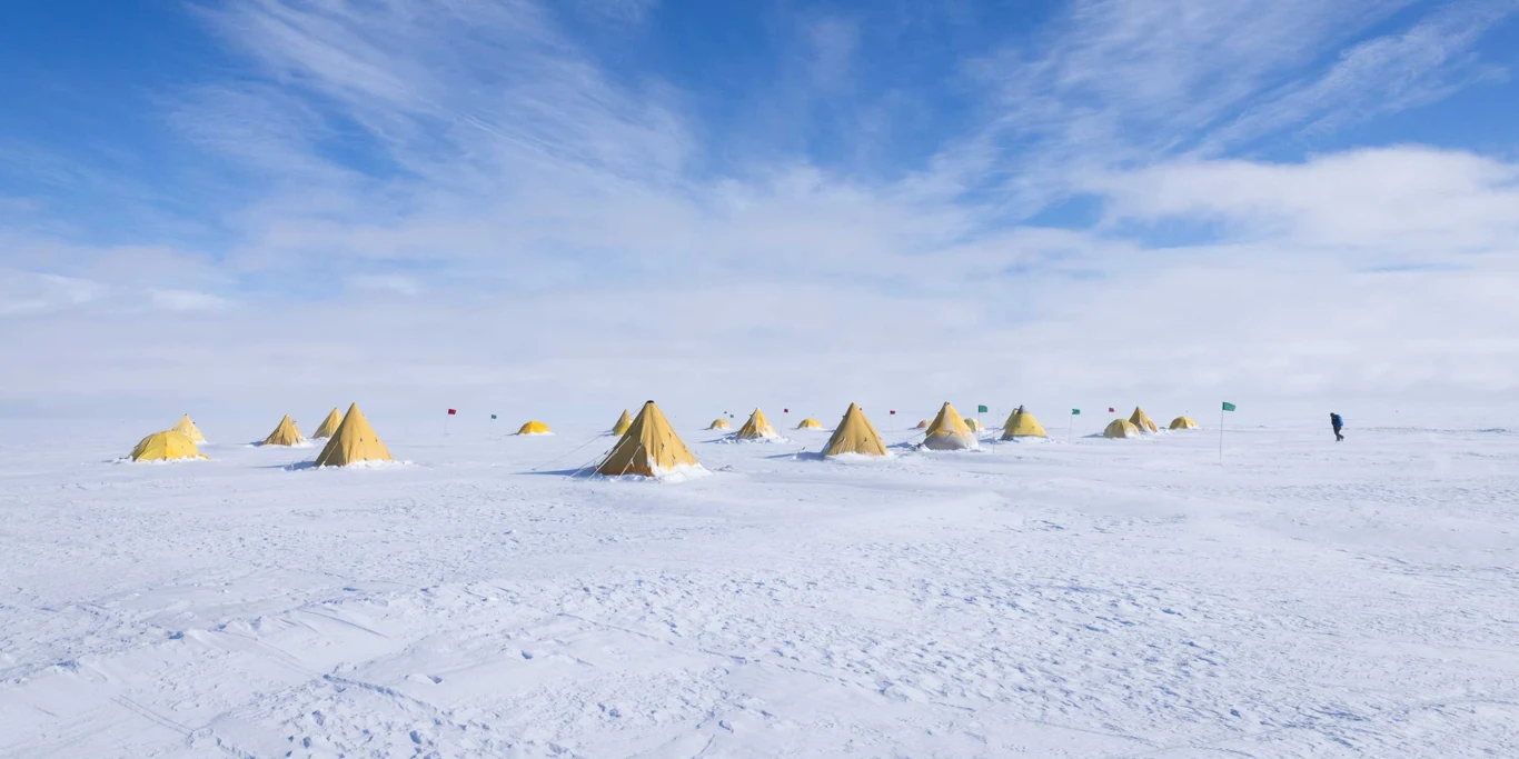 Przez dwa miesiące zespół badaczy z dziesięciu krajów mieszkał i pracował w odległym obozie terenowym w Antarktydzie Zachodniej Rząd żółtych namiotów rozstawionych na śnieżnej, rozległej przestrzeni z błękitnym niebem i pojedyńczą osobą w oddali po prawej stronie.