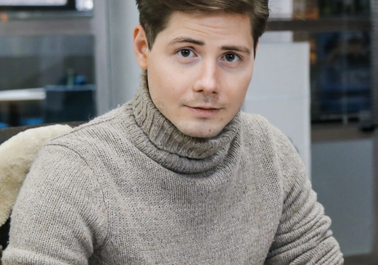 Piotr Bondyra Młody mężczyzna o jasnych włosach siedzi przy biurku, ubrany w szary golf z grubego materiału, patrzy spokojnie w stronę aparatu.