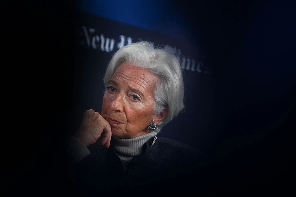 Szefowa Europejskiego Banku Centralnego Christine Lagarde Starsza kobieta z siwymi włosami siedzi zamyślona z ręką opartą o brodę, ubrana elegancko w ciemny sweter i duże kolczyki, ciemne tło z niewyraźnym napisem.