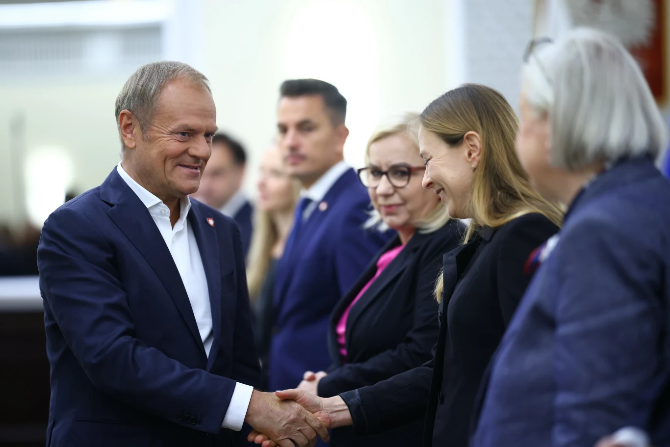 Co po rozpadzie Polski 2050 zrobi premier Donald Tusk? Mężczyzna w garniturze uśmiecha się i podaje rękę kobiecie, obok stoi grupa osób w oficjalnych strojach, atmosfera jest uprzejma i formalna.