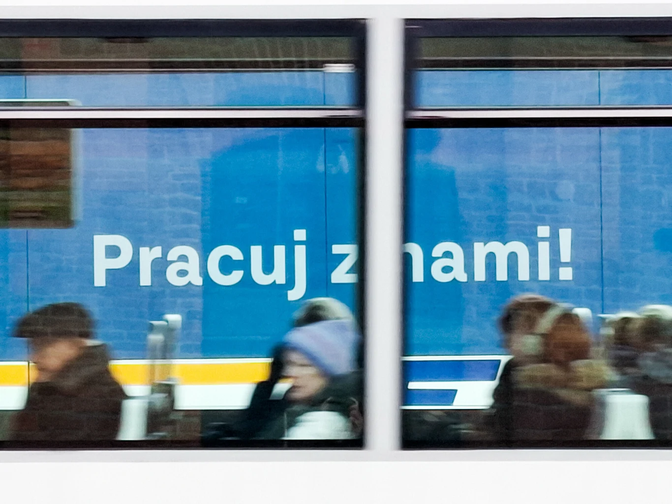 Bezrobocie w Polsce wzrosło w styczniu 2026 r. do 6 proc., co oznacza najwyższy miesięczny wzrost od dwóch lat. Niebieski autobus lub tramwaj z reklamą i napisem 'Pracuj z nami!', przez okno widać zamazane sylwetki kilku osób siedzących w środku, ubrani w zimowe ubrania.
