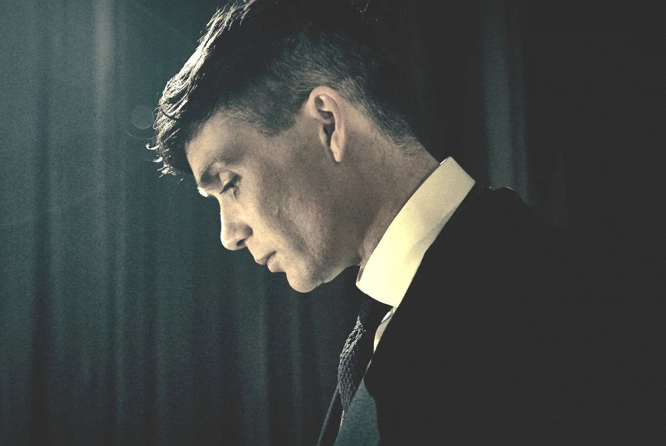 "Peaky Blinders": Cillian Murphy jako Tommy Shelby Cillian Murphy jako Tommy Shelby w garniturze, profil, głowa pochylona, oświetlenie z góry, scena z filmu "Peaky Blinders".