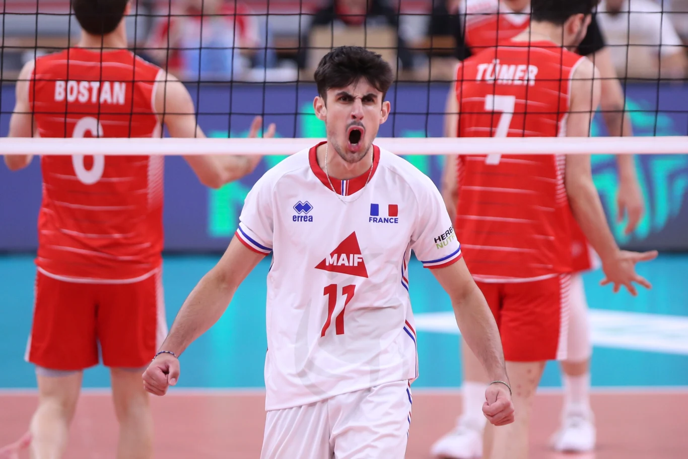 Antoine Pothron w 2022 roku zagrał na mistrzostwach Europy do lat 22 Zawodnik drużyny Francji w białym stroju z numerem 11 okazujący silne emocje, w tle przeciwnicy w czerwonych strojach po drugiej stronie siatki, dynamiczna scena podczas meczu siatkówki.