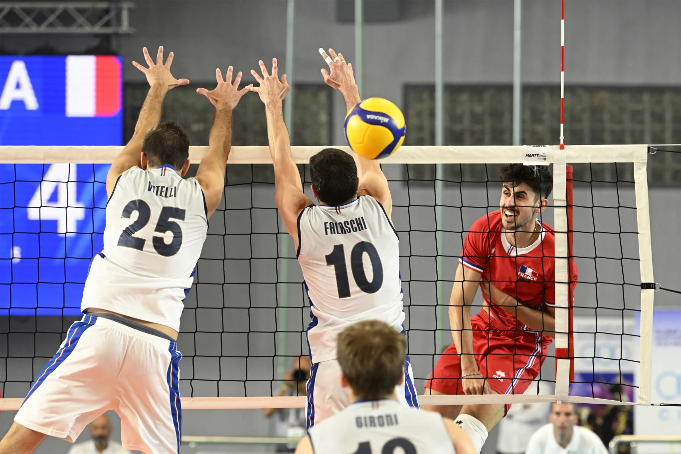 Antoine Pothron podczas występu na ME do lat 22 Dwóch zawodników w białych strojach próbuje zablokować atakującego siatkarza w czerwonym stroju, piłka znajduje się nad siatką, a w tle widoczni są pozostali uczestnicy meczu siatkówki.