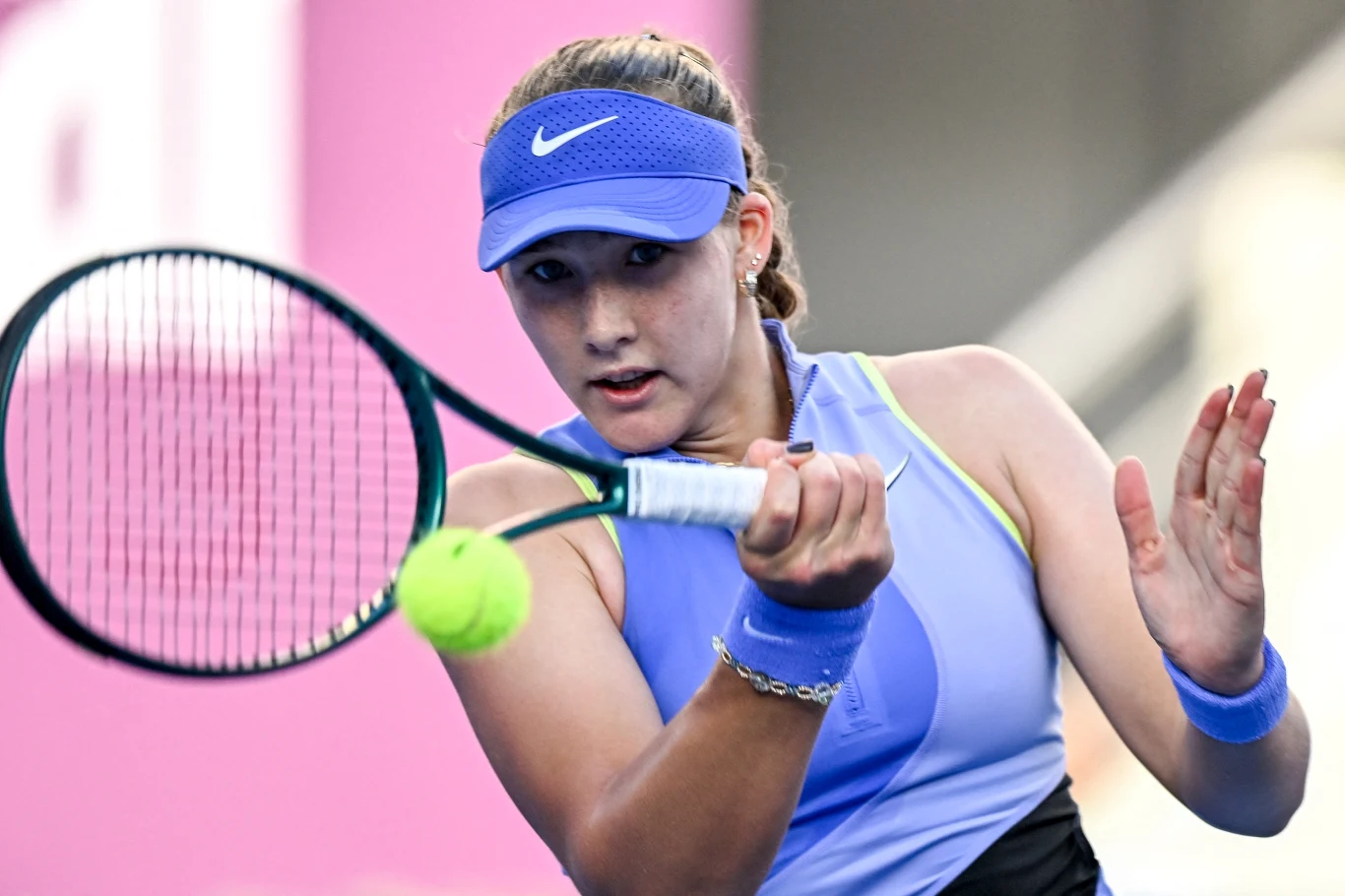 Mirra Andriejewa Zbliżenie na młodą tenisistkę w niebieskim stroju sportowym podczas gry, skupiona na odbiciu piłki tenisowej rakietą.