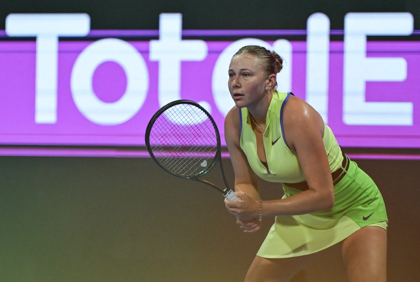 Amanda Anisimova Tenisistka w żółto-zielonym stroju przygotowuje się do odbioru piłki podczas meczu na krytym korcie, w tle widoczna reklama.