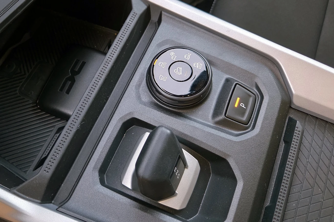 Panel sterowania samochodu terenowego z okrągłym pokrętłem do wyboru trybu jazdy, przyciskiem blokady oraz dźwignią zmiany napędu.