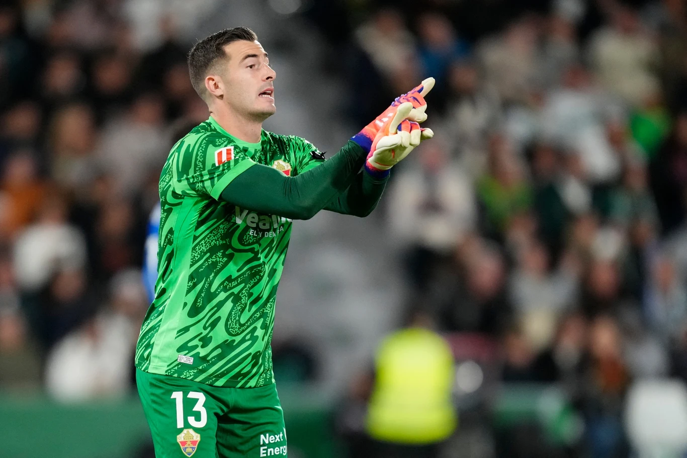 Inaki Pena Bramkarz w zielonym stroju z numerem 13 wykonuje gesty ręką, stojąc na tle rozmytej publiczności na stadionie.
