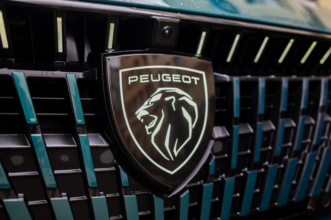 Emblemat marki Peugeot z wizerunkiem lwa umieszczony na czarnym grillu samochodowym z wyrazistymi geometrycznymi detalami.