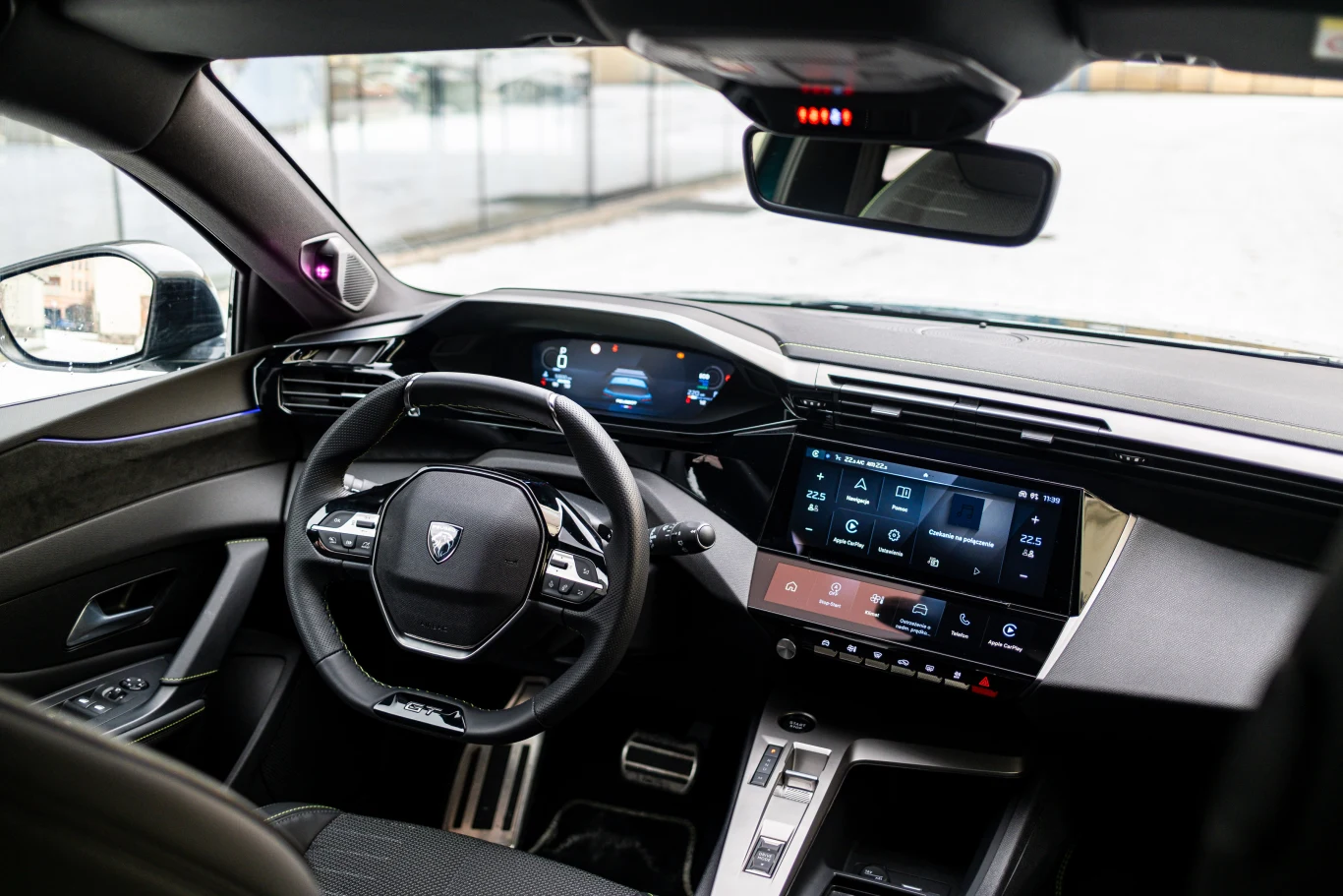 Nowoczesne wnętrze samochodu z cyfrowym kokpitem, dużym, dotykowym ekranem multimedialnym, kierownicą z logiem producenta oraz elegancką deską rozdzielczą.