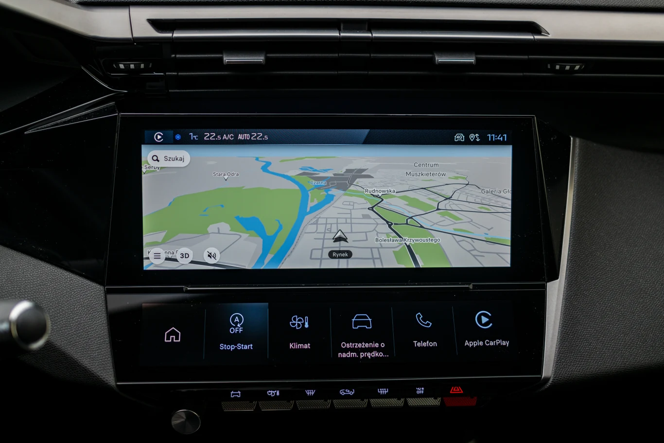 Ekran dotykowy systemu multimedialnego w samochodzie z wyświetloną mapą nawigacji, widoczne opcje takie jak Start-Stop, Klimat, ostrzeżenia o niebezpieczeństwie, telefon oraz Apple CarPlay.