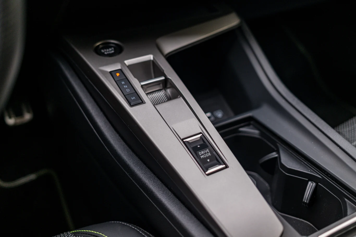 Konsola środkowa nowoczesnego samochodu z przyciskiem uruchamiania silnika, selektorem trybu jazdy oraz miejscem na napoje.