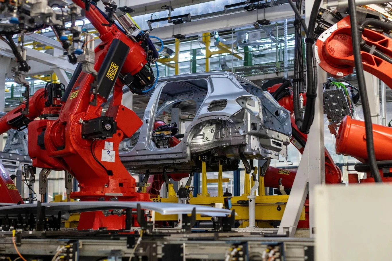 Za niedobory pamięci odpowiada sztuczna inteligencja Czerwone ramiona robotów przemysłowych pracujące przy składaniu nadwozia samochodu na linii produkcyjnej w fabryce, otoczenie w nowoczesnej hali pełnej technologicznych urządzeń.