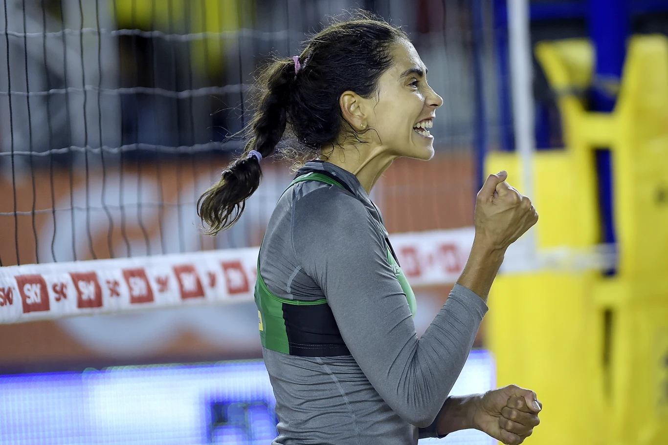 Carolina Solberg Salgado Kobieta w sportowym stroju na tle siatki do siatkówki, z zaciśniętą pięścią i szerokim uśmiechem na twarzy, wyrażająca silne emocje, najprawdopodobniej po udanej akcji podczas meczu siatkówki plażowej.