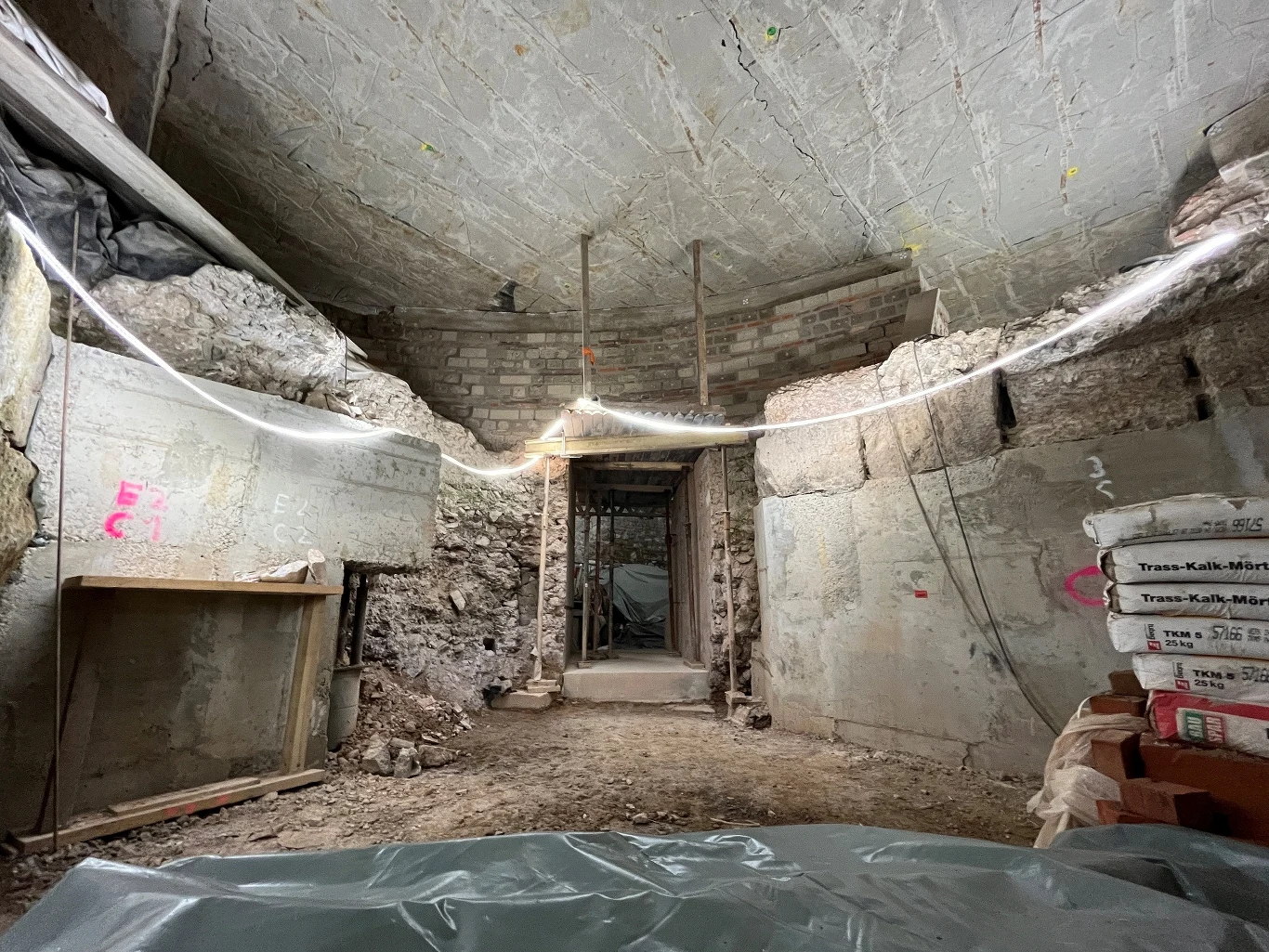 Bazylika, lararium i schody do Renu. Archeolodzy odsłaniają "ukryte" rzymskie miasto sprzed 2 tys. lat Surowe wnętrze betonowego schronu lub tunelu w trakcie remontu, z wystawionymi workami cementu po prawej stronie, stertą materiałów budowlanych po lewej i plastikową folią na podłodze.