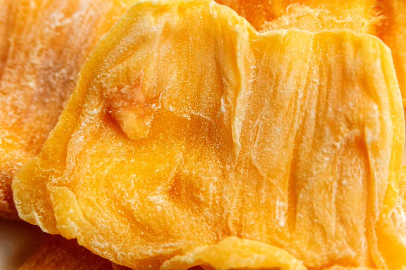 Suszone plastry mango o intensywnie żółtopomarańczowej barwie, o charakterystycznej teksturze miąższu.
