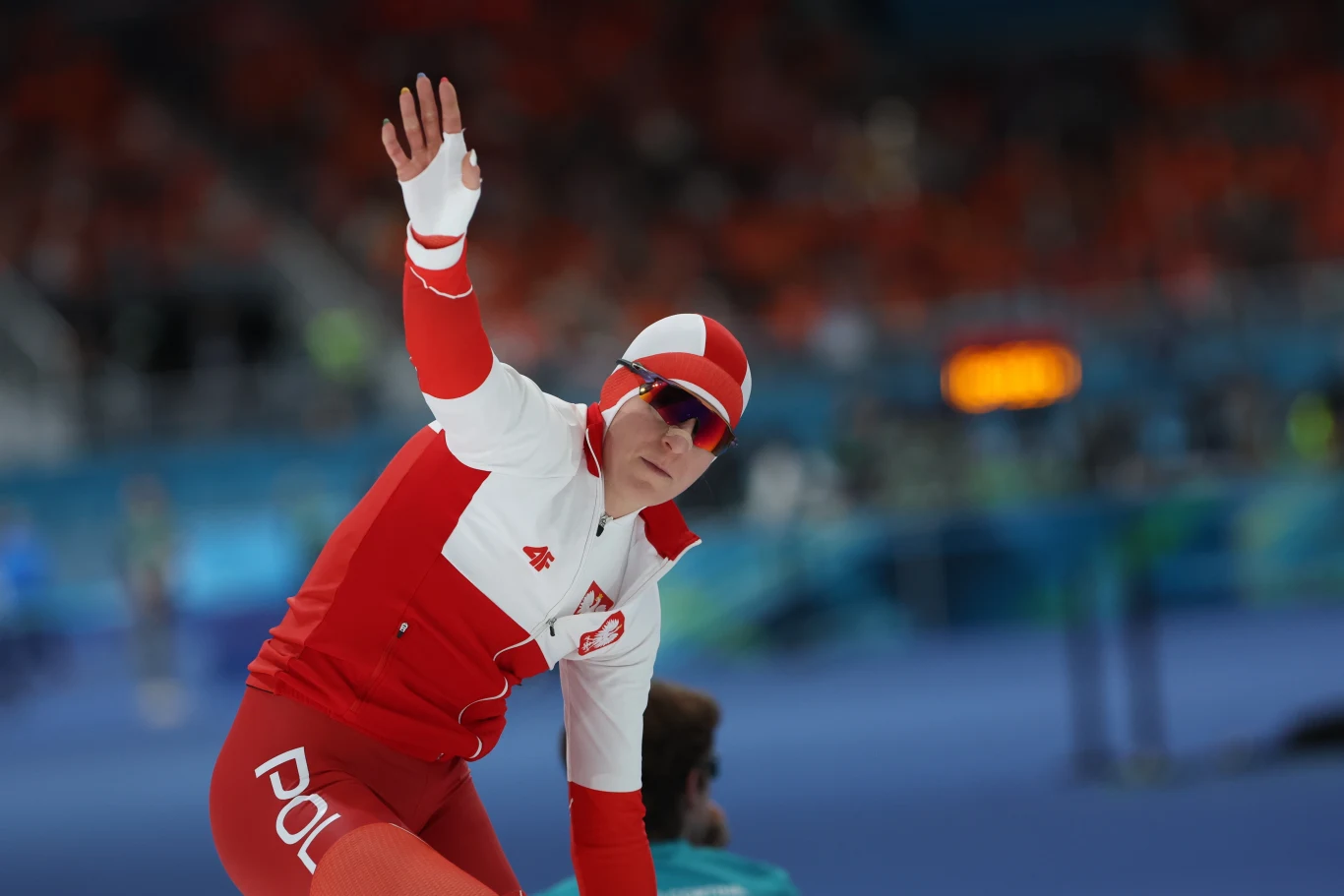 Zawodnik w stroju reprezentacji Polski do łyżwiarstwa szybkiego wykonuje gest ręką, znajdując się na lodowisku podczas zawodów sportowych.