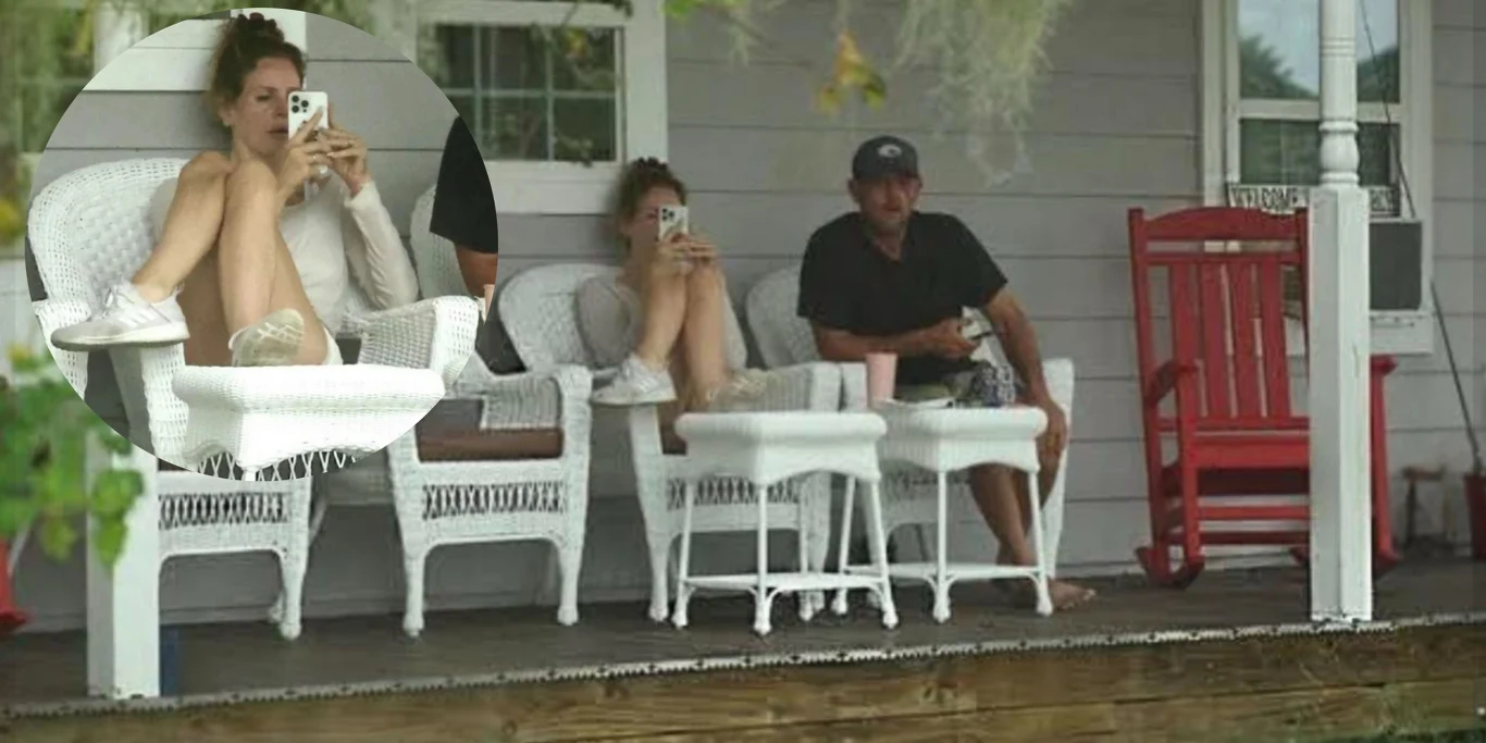 Troje ludzi siedzi na białych wiklinowych krzesłach na werandzie domu. Dwie osoby korzystają z telefonów komórkowych, trzecia opiera się, patrząc na zewnątrz. Obok nich stoi czerwony bujany fotel.