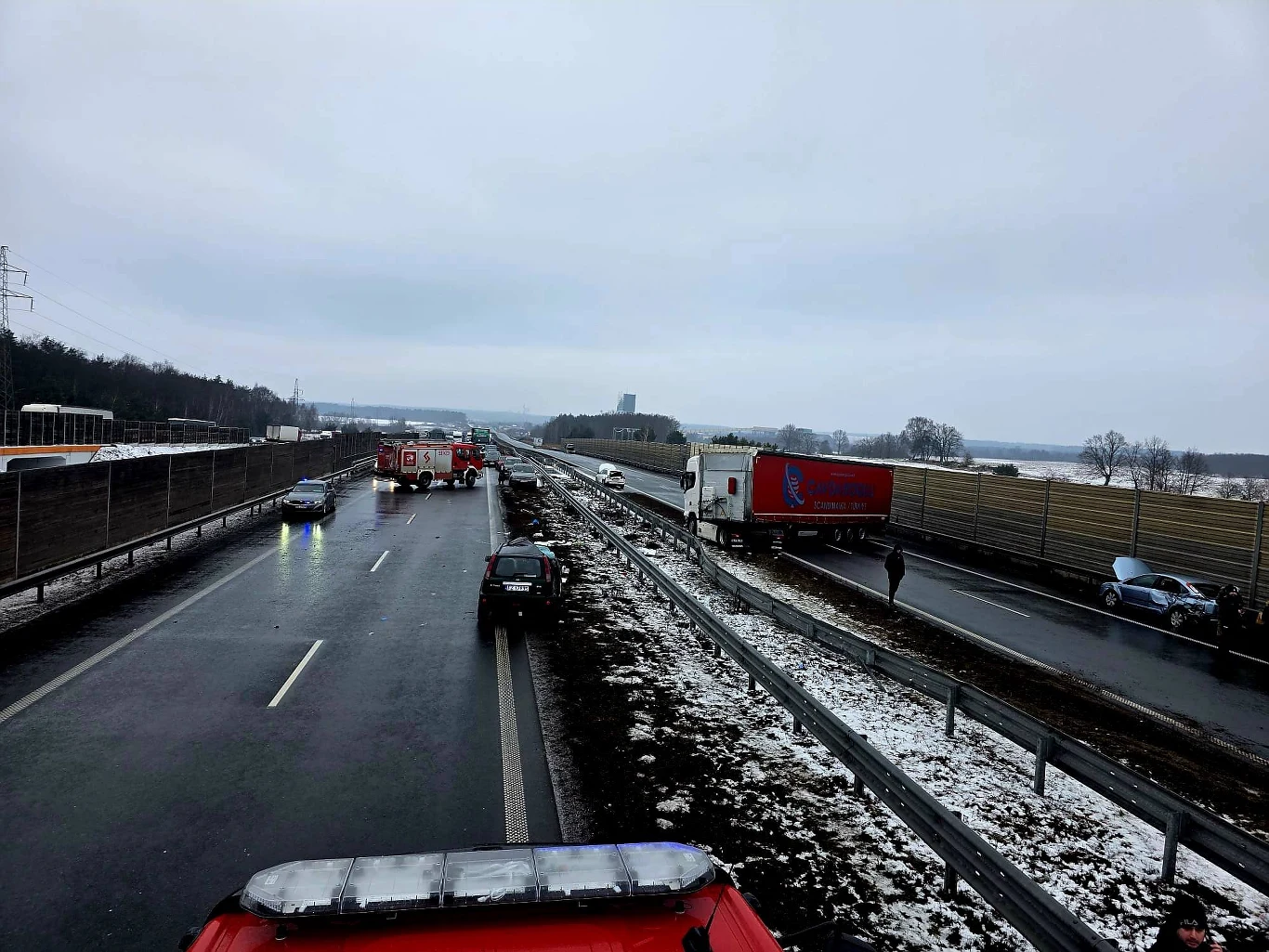 Kolizja drogowa na autostradzie z udziałem kilku pojazdów, w tym samochodu ciężarowego oraz samochodów osobowych. Na miejscu obecne są służby ratunkowe i straż pożarna, ruch w jednym kierunku został zatrzymany. Droga jest śliska, obok leży rozjeżdżony ...