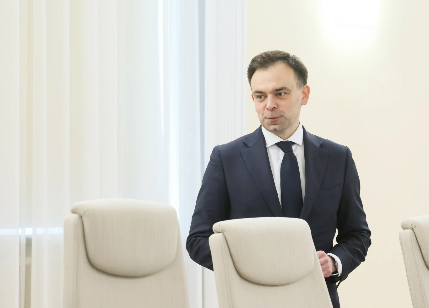 Minister o programie SAFE: To do 60 mld zł oszczędności na modernizacji armii Mężczyzna w garniturze stoi w jasnym, nowoczesnym pomieszczeniu, otoczony jasnymi krzesłami biurowymi. Na jego twarzy widoczny jest poważny wyraz.