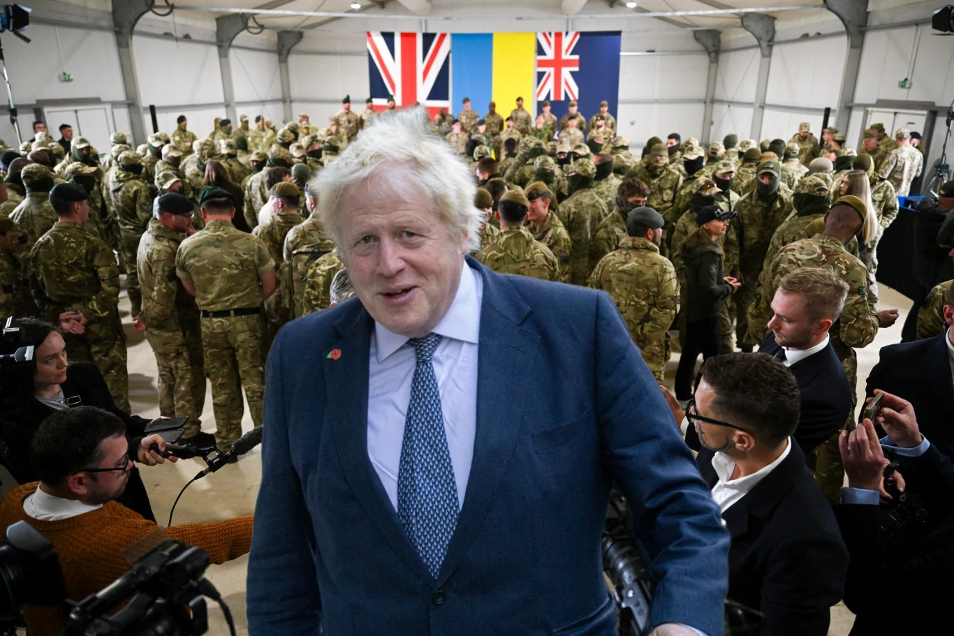 Były premier Wielkiej Brytanii mówił o wysłaniu wojsk na Ukrainę Premier Wielkiej Brytanii stoi na pierwszym planie wśród grupy żołnierzy w mundurach, w tle widoczne są trzy flagi: brytyjska, ukraińska oraz kolejna brytyjska, wokół zgromadzeni są przedstawiciele mediów z kamerami.