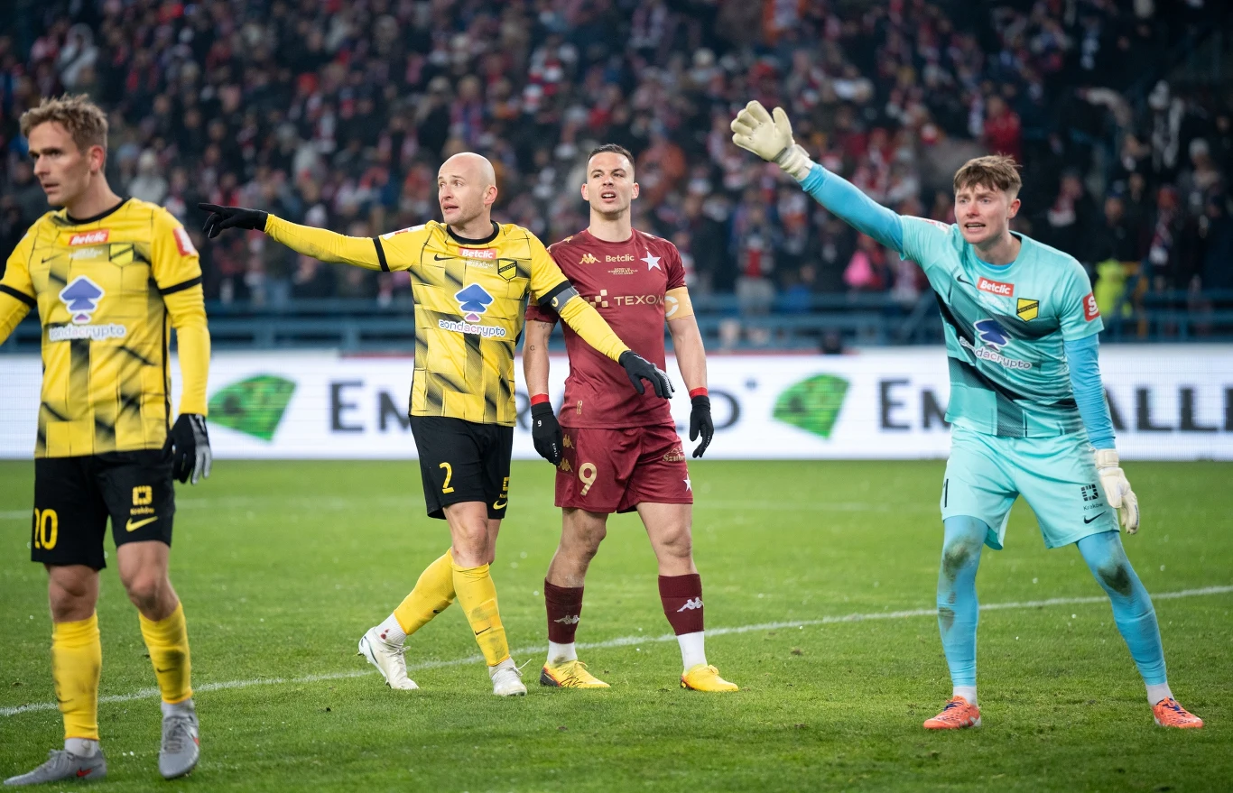 Michał Pazdan i Angel Rodado Piłkarze dwóch drużyn rywalizujących podczas meczu na stadionie, w tym bramkarz w turkusowym stroju i kilku zawodników ubranych w żółto-czarne stroje z jasnożółtymi elementami oraz zawodnik w bordowym stroju na tle licznej publiczności.