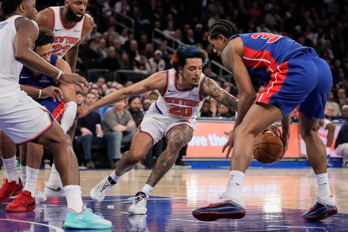 Zawodnik drużyny New York Knicks stara się odebrać piłkę koszykarzowi z Detroit Pistons podczas meczu koszykówki, otoczony przez innych graczy obu drużyn na tle trybun pełnych kibiców.