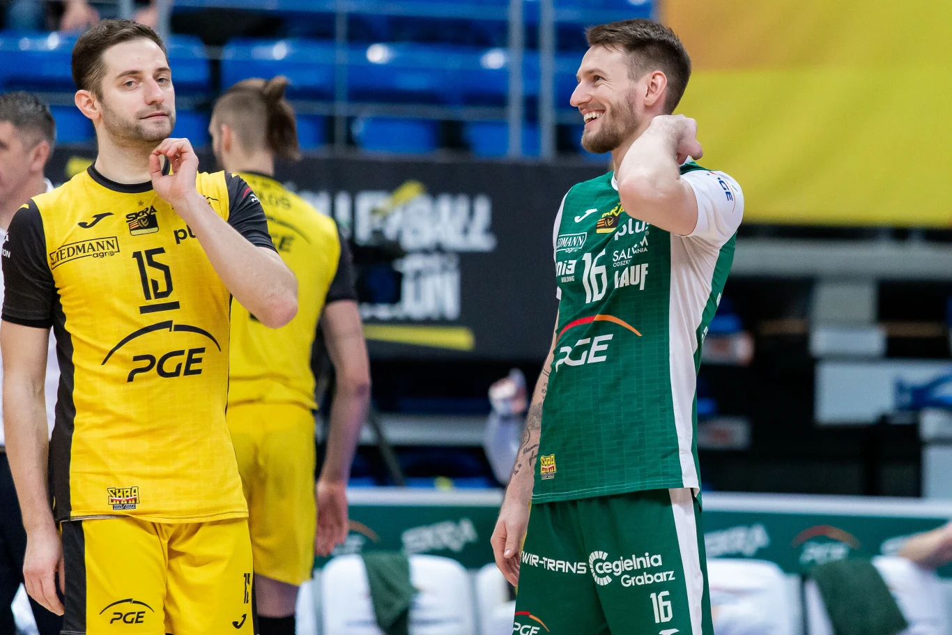 Kacper Piechocki rozstał się ze Skrą Bełchatów w połowie 2023 roku Dwóch siatkarzy w strojach sportowych stoi na boisku i rozmawia, jeden ubrany w żółty strój, drugi w zielony, wokół widoczne są trybuny, a w tle banery sponsorów.