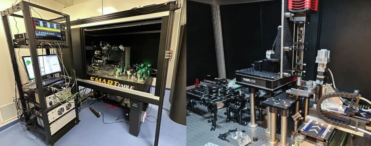 Zaawansowane stanowiska laboratoryjne wyposażone w skomplikowane urządzenia elektroniczne i optyczne, na blatach widoczne są liczne przewody, lasery oraz elementy mechaniczne, całość otoczona jest metalowymi i plastikowymi konstrukcjami oddzielającymi ...