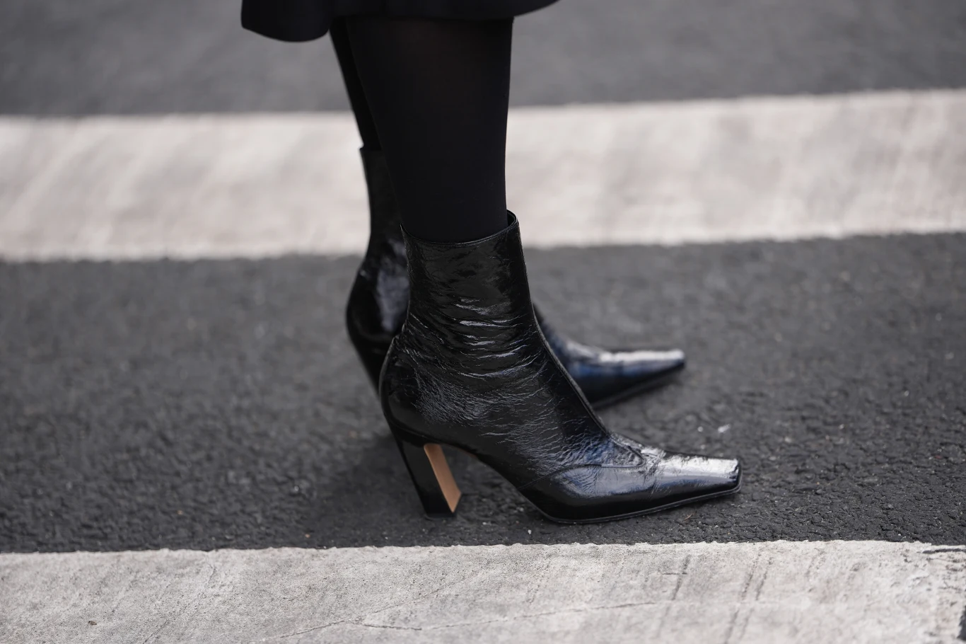 Czarne, lakierowane botki na obcasie na tle pasów przejścia dla pieszych.