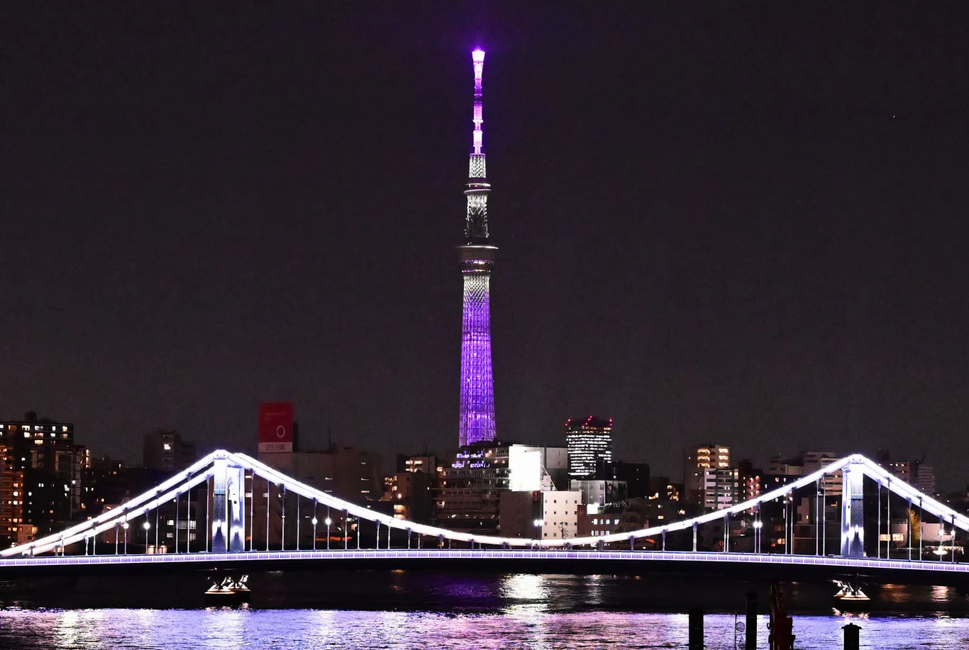 Na wieży widokowej Tokyo Skytree doszło do awarii windy Podświetlony most rozciąga się nad rzeką, na tle nowoczesnej miejskiej zabudowy wieżowiec z wysoką, wyróżniającą się wieżą w barwach fioletowo-białych.