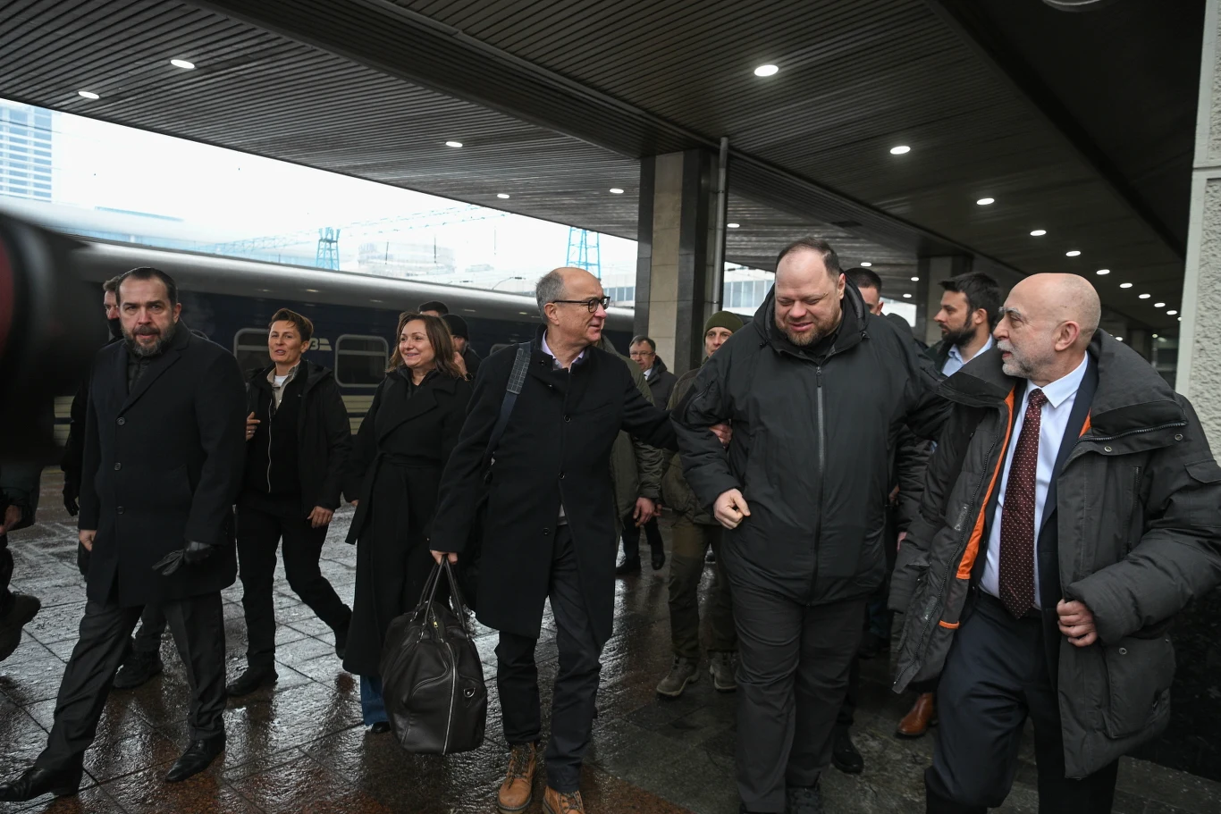 Marszałek Sejmu Włodzimierz Czarzasty oraz przewodniczący Rady Najwyższej Ukrainy Rusłan Stefanczuk podczas powitania na dworcu kolejowym w Kijowie Grupa osób ubranych w płaszcze i kurtki idąca po chodniku pod zadaszeniem przy peronie kolejowym, w tle widać wagon pociągu oraz fragment budynku.