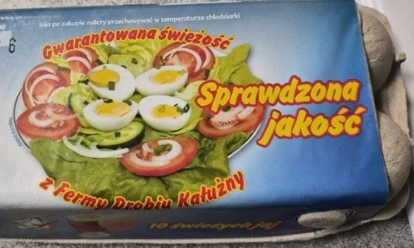 Opakowanie jajek z nadrukowanym zdjęciem sałatki składającej się z plasterków jajek na twardo, pomidorów, ogórków i liści sałaty, otoczone kolorowymi napisami reklamowymi gwarantującymi świeżość i jakość produktu.