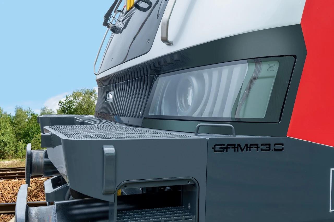 Nowa lokomotywa GAMA 3.0 dla PKP Intercity przyjechała na testy. Nowoczesna lokomotywa GAMA 3.0 z wyraźnie widocznymi reflektorami oraz elementami konstrukcyjnymi z przodu, na tle niebieskiego nieba i zieleni.