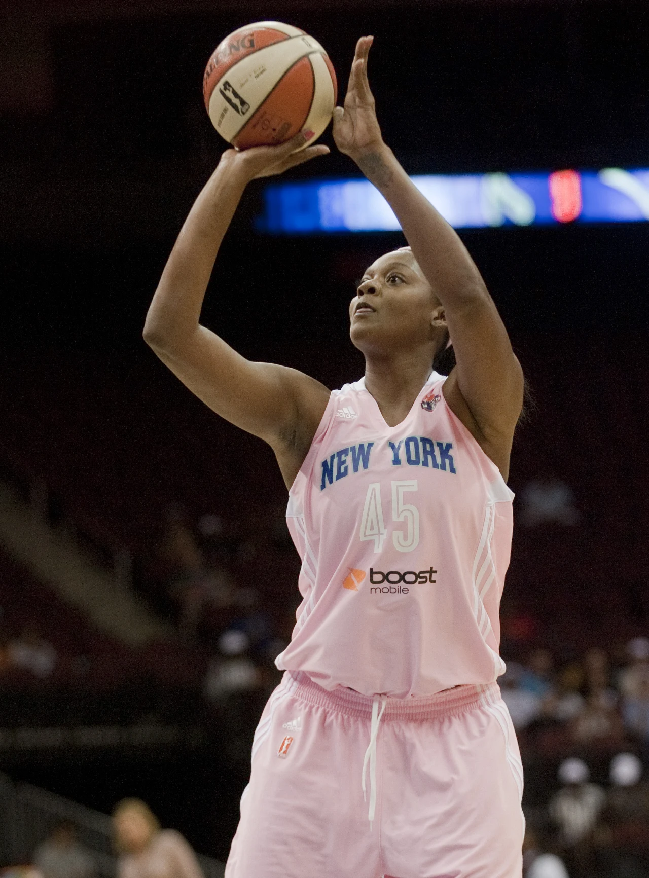 Koszykarka w różowym stroju drużyny New York przygotowuje się do rzutu wolnego, trzymając piłkę ponad głową w dynamicznej pozie na boisku sportowym.