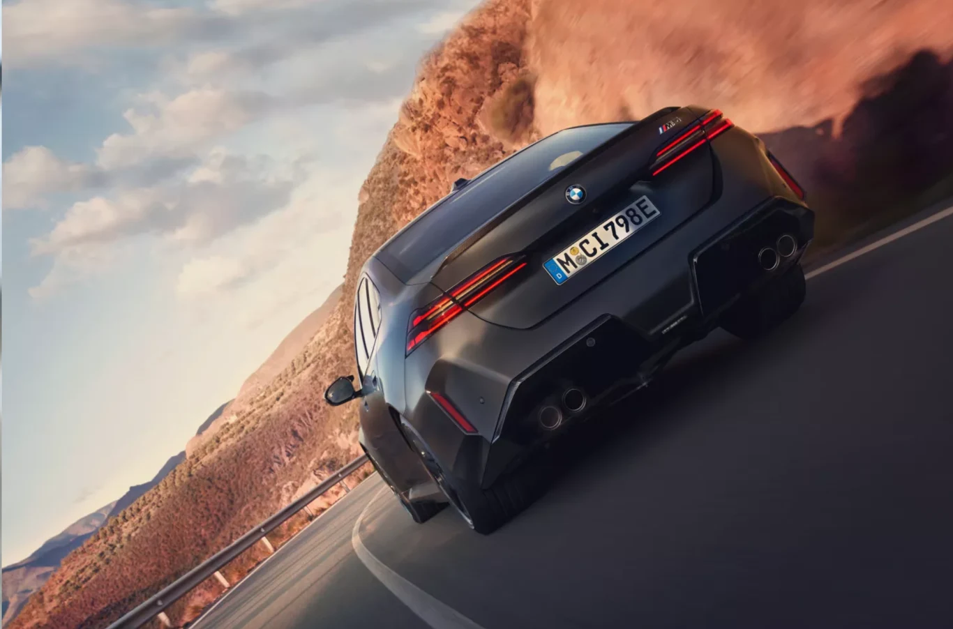 Aktualny cennik pokazuje, że kwoty rozpoczynają się od około 614 tys. zł, a w przypadku bogatszych wersji mogą sięgać nawet 699 tys. zł. Nowoczesny sportowy samochód BMW w ciemnym kolorze porusza się dynamicznie po krętej, górskiej drodze, otoczonej skalnymi zboczami i jasnym niebem.
