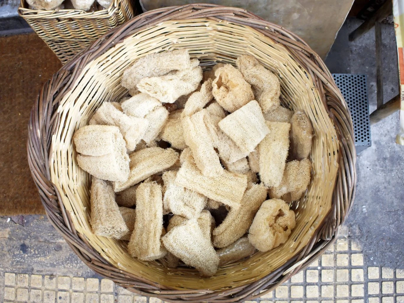 Kosz wypełniony naturalnymi gąbkami roślinnymi o jasnobeżowej barwie, ułożonymi w wiklinowym koszu.