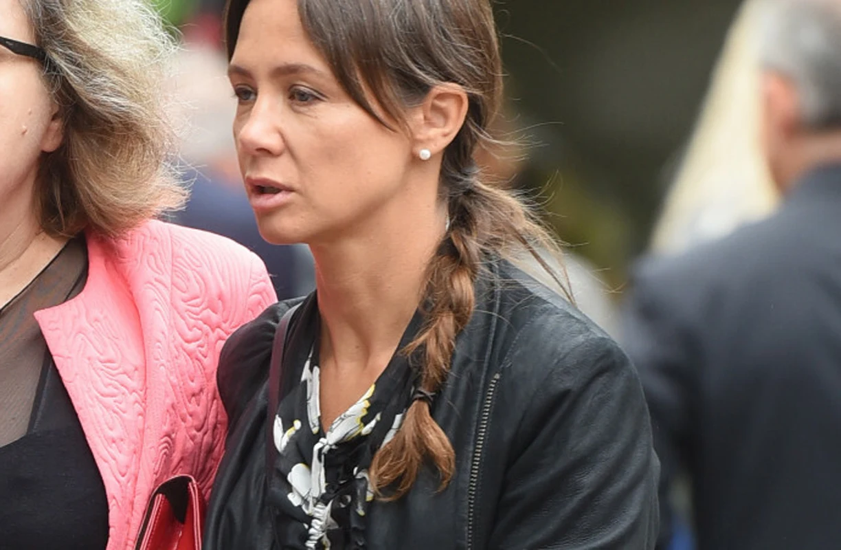 Kinga Rusin Kobieta z ciemniejszymi włosami splecionymi w warkocz, ubrana w czarną kurtkę i jasną bluzkę z wzorem kwiatowym, idąca obok drugiej osoby w różowym płaszczu.