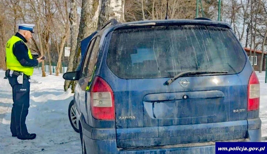 W ramach prowadzonej akcji policja kontrolowała nie tylko samochody nadające się do driftowania Policjant w kamizelce odblaskowej kontroluje niebieski samochód marki Opel zaparkowany na śniegu, w tle drzewa i zabudowania, zimowa sceneria.