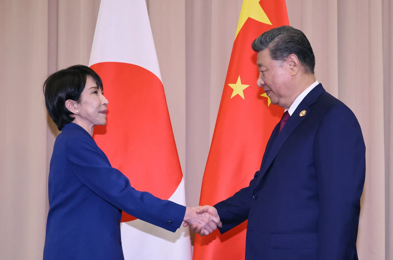 Premier Japonii Sanae Takaichi oraz przywódca Chin Xi Jinping Dwóch polityków wymienia uścisk dłoni przed flagami Japonii i Chin podczas oficjalnego spotkania.