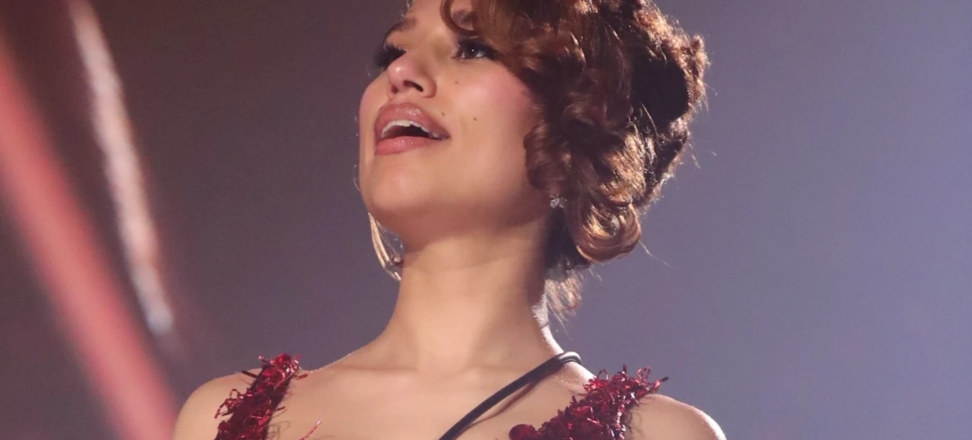 RAYE Kobieta w eleganckiej czerwonej sukni z upiętymi włosami śpiewa na scenie, oświetlona ciepłym światłem.