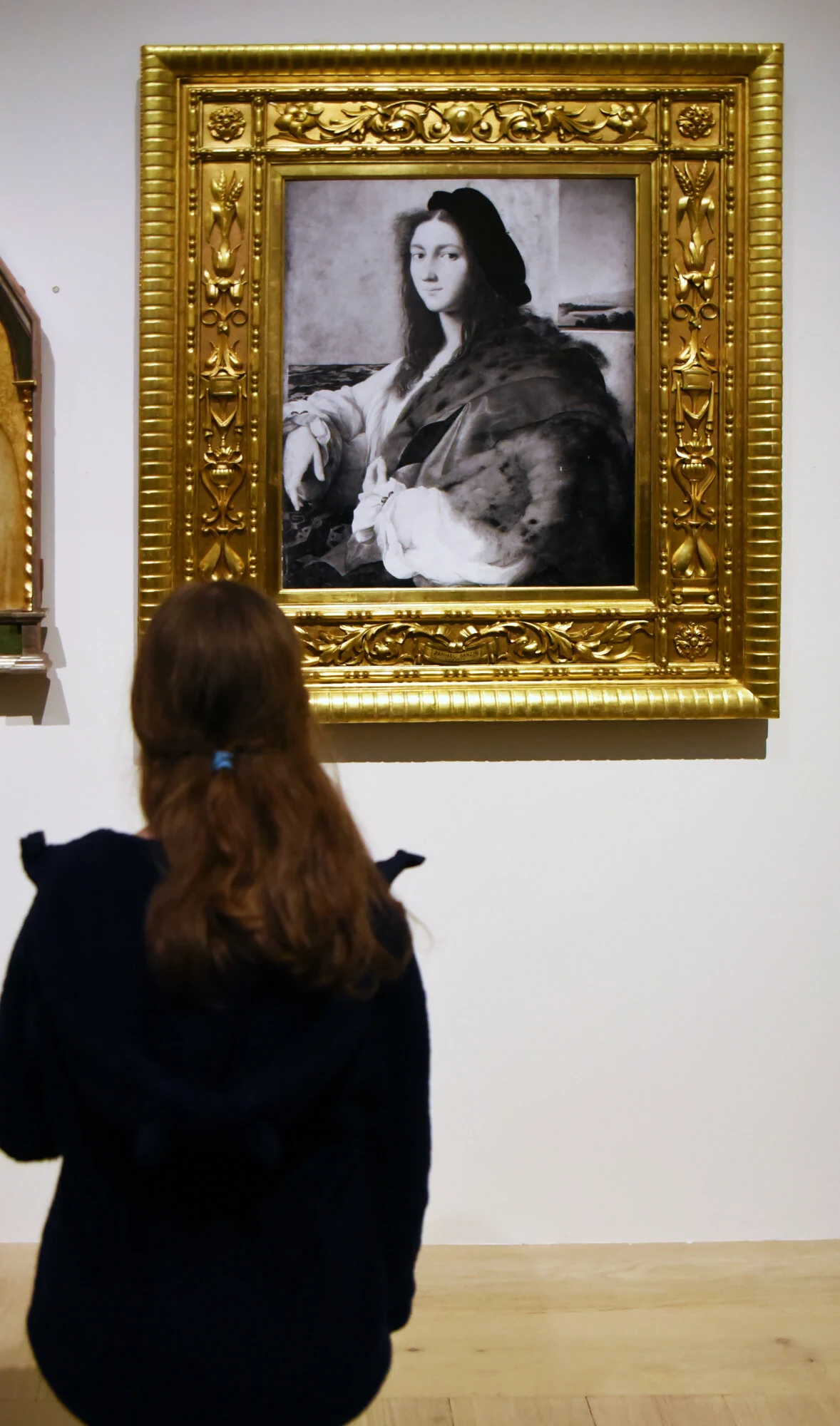 "Portret młodzieńca" został zrabowany przez Niemców w czasie II wojny światowej Dziewczynka z długimi włosami stojąca tyłem podziwia w muzeum obraz kobiety w bogatej sukni, oprawiony w złoconą ramę.