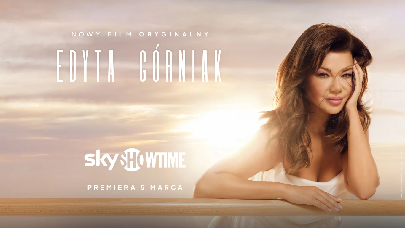 Edyta Górniak uśmiecha się, opierając się na ręku, na tle jasnego nieba, z napisami zapowiadającymi premierę oryginalnego filmu na platformie SkyShowtime.